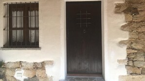 A rustic building with a dark wooden door, a window with bars, and a stone wall. - Cottage in Sardegna Barbagia (Fonni)