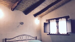 A bedroom with a metal bed frame, a single bed with a green bedspread, a small window with curtains, and a wall-mounted light fixture. - Cottage in Sardegna Barbagia (Fonni)