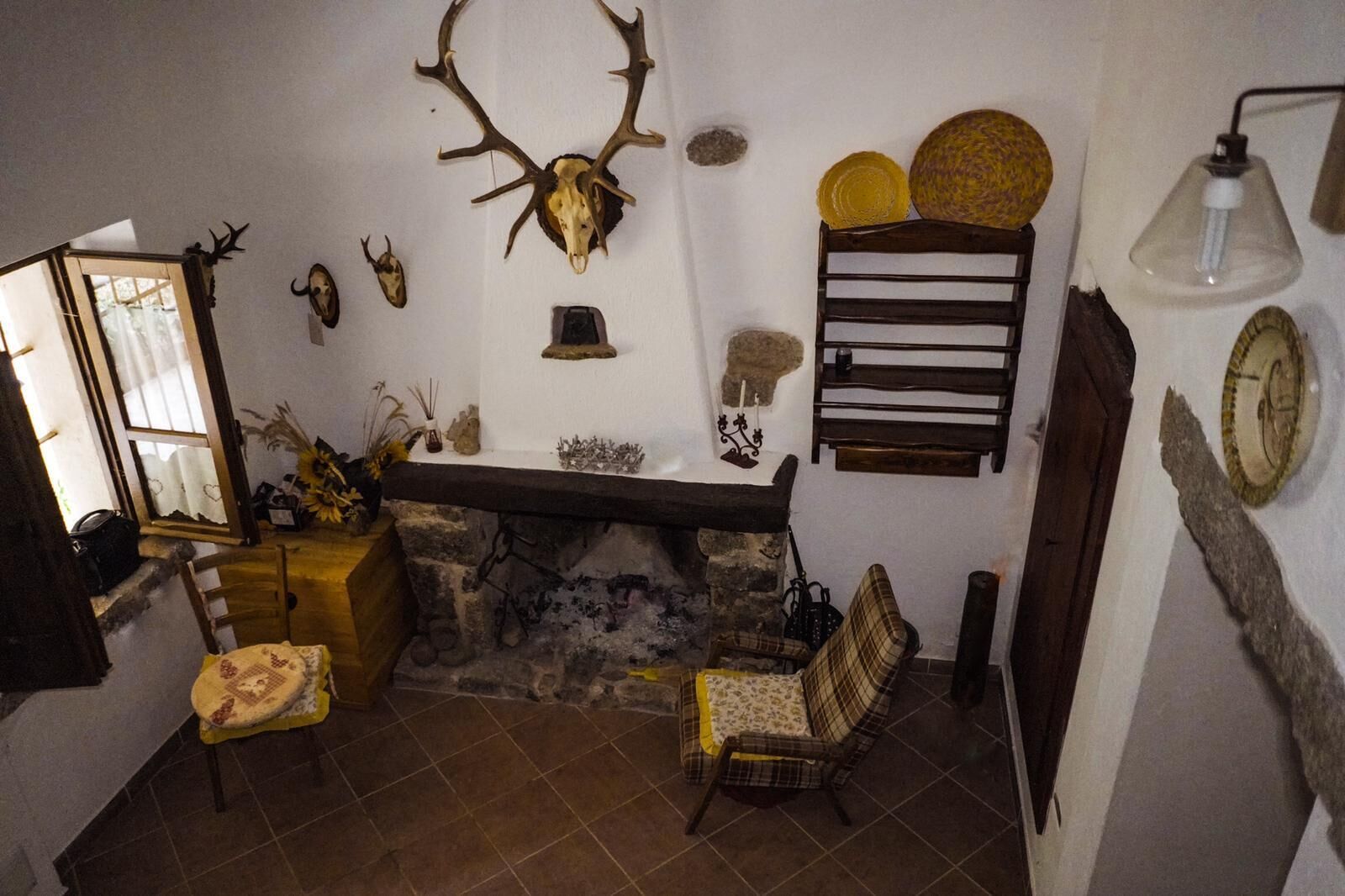 Ein rustikales Interieur mit Kamin aus Stein, Holzböden und verschiedenen Dekorationsobjekten, darunter Tierpräparate und eine Uhr.