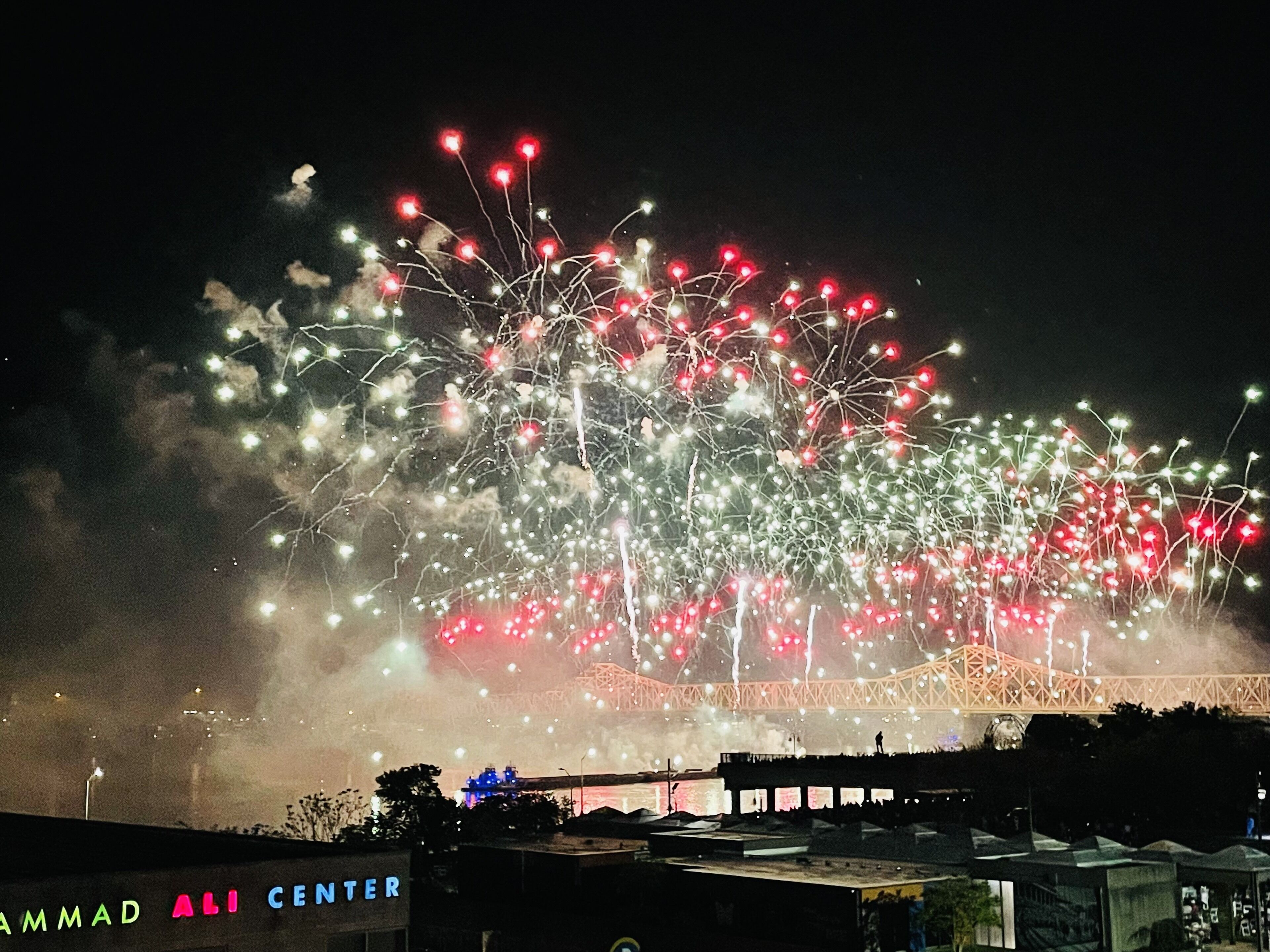 A fireworks display over a bridge with a sign reading "Ali Center".