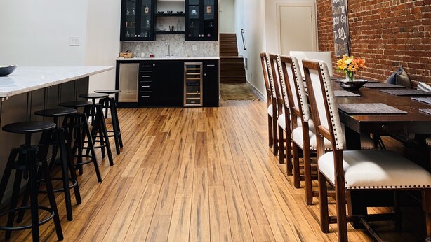 A modern kitchen with a skylight, wooden flooring, and a dining area with chairs and a table.