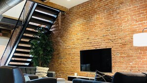 A modern living room with a brick wall, a flat-screen TV, leather sofas, and a staircase.