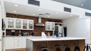 A modern kitchen with white cabinetry, a brick accent wall, stainless steel appliances, and a central island with bar stools.