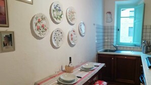 Une cuisine avec une table à manger dressée pour quatre personnes, une fenêtre donnant sur un beau paysage et plusieurs assiettes décoratives accrochées au mur.