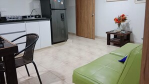 Un espacio habitable compacto con kitchenette, comedor y sofá verde.