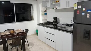 Una cocina moderna con armarios blancos, encimera negra, refrigerador y un comedor con mesa y sillas.