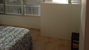 Un dormitorio con cama, una ventana que ofrece vistas a un paisaje urbano y una mesita.