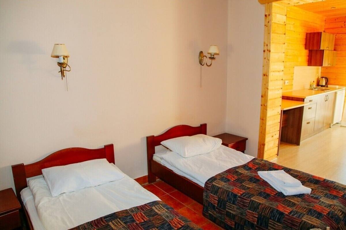 A room with two beds, a small desk, and a kitchenette.