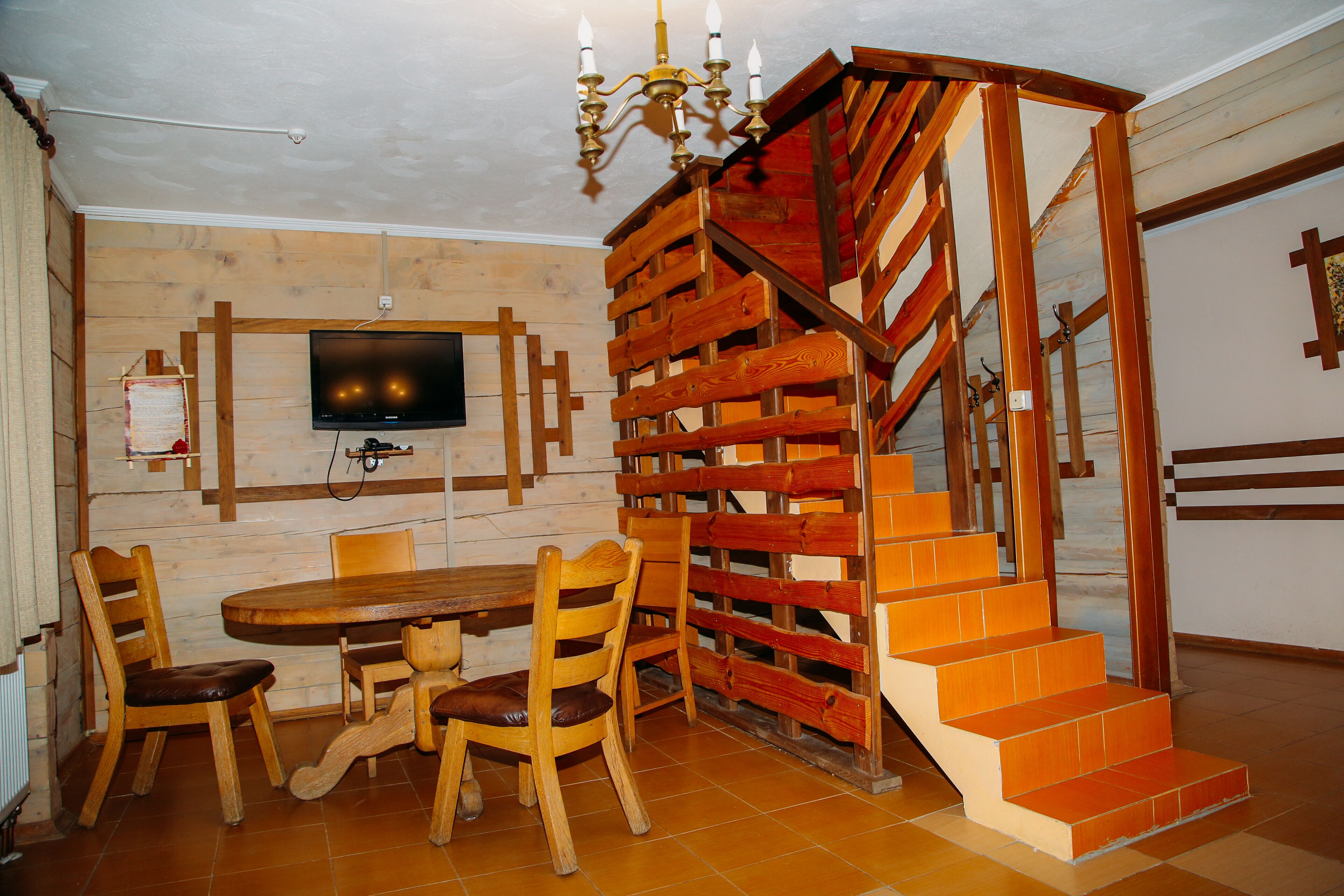 A dining area with a wooden table and chairs, a TV mounted on the wall, and a wooden staircase.