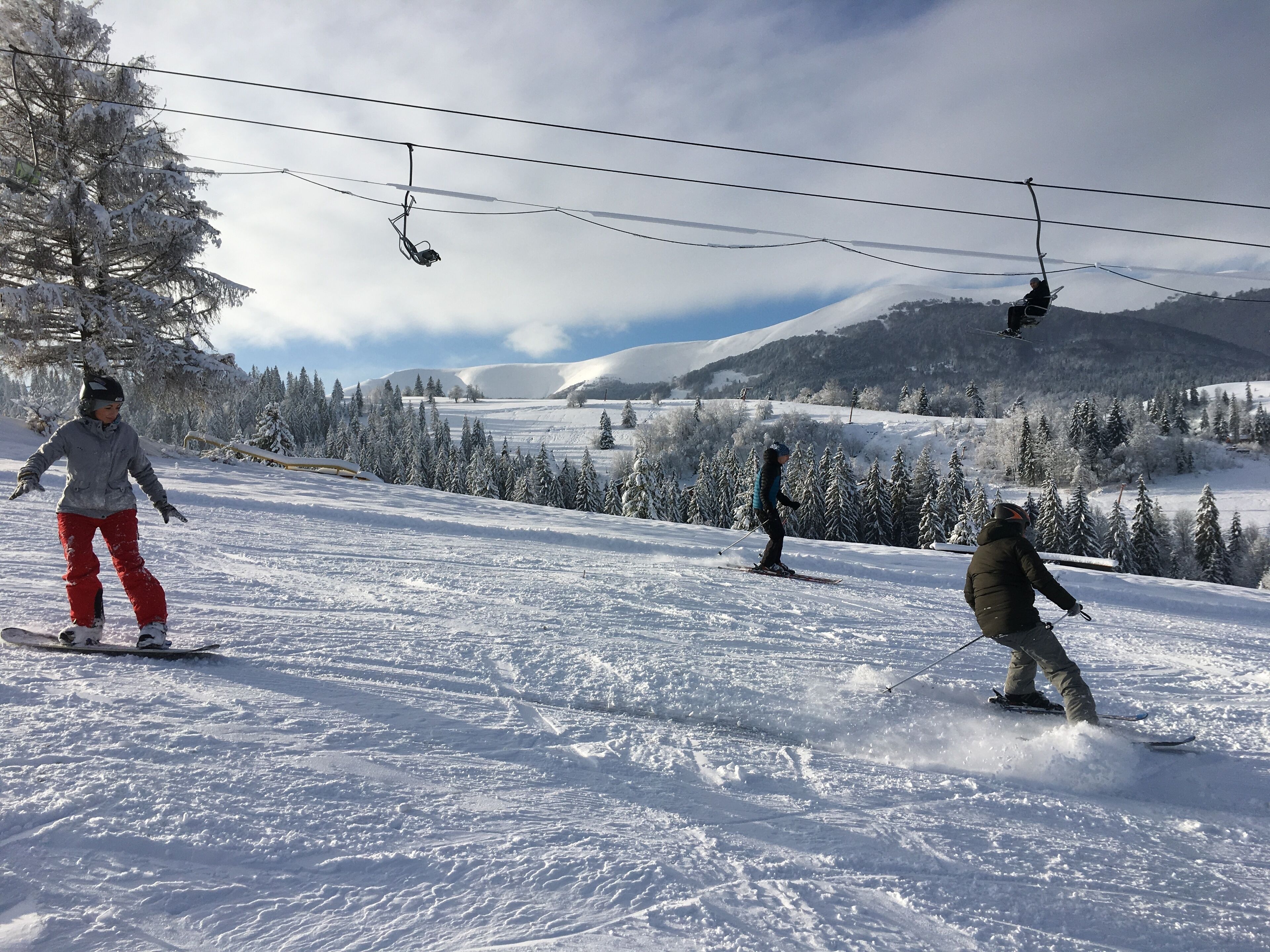 A ski slope with skiers, a ski lift, and snow-covered trees.