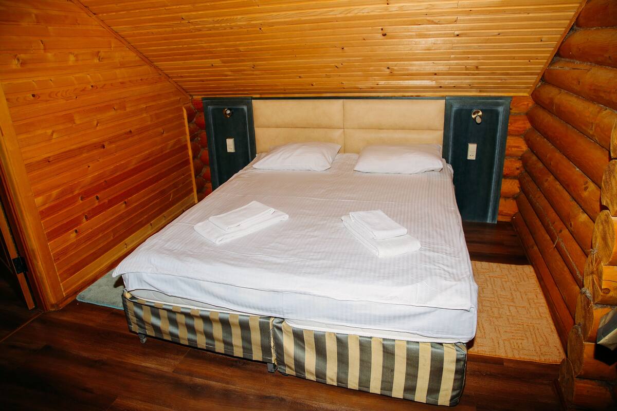 A wooden cabin bedroom with a bed, two nightstands, and a wooden ceiling.