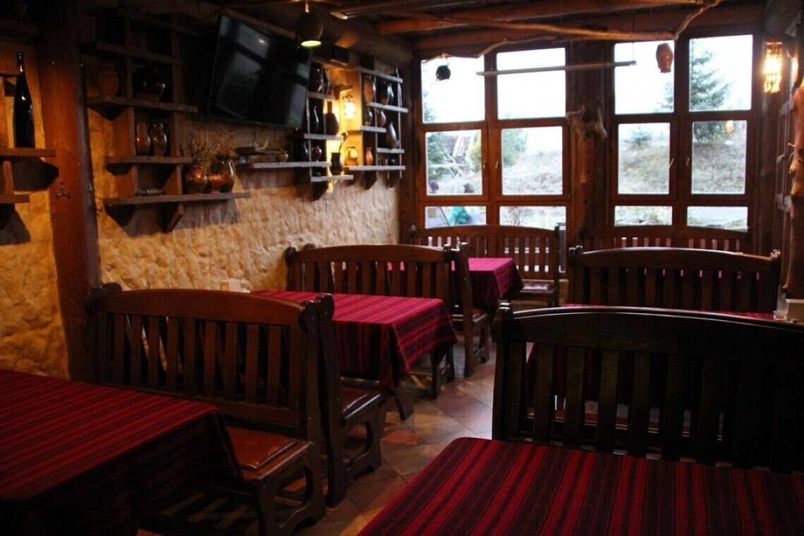 A rustic interior with wooden tables and benches, stone walls, and a television mounted on the wall.
