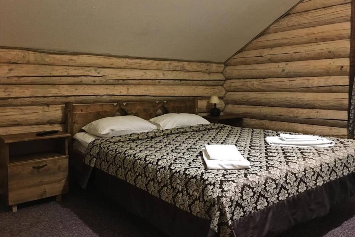 A log cabin bedroom with a bed, two pillows, a nightstand, and a drawer.