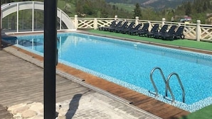 A swimming pool with a wooden deck, lounge chairs, and a view of a mountainous landscape. - Eco-resort Izki (Izky)