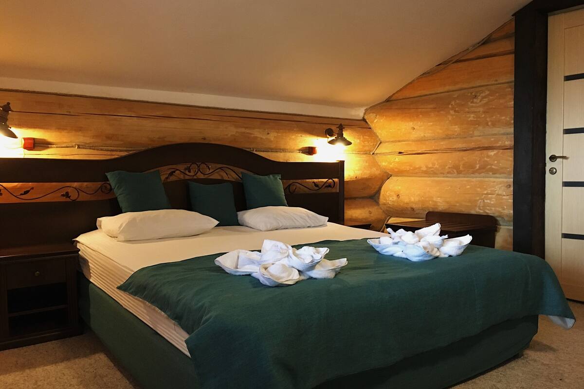 A neatly made bed with a green bedspread and white pillows, a wooden headboard, and a nightstand with a lamp.