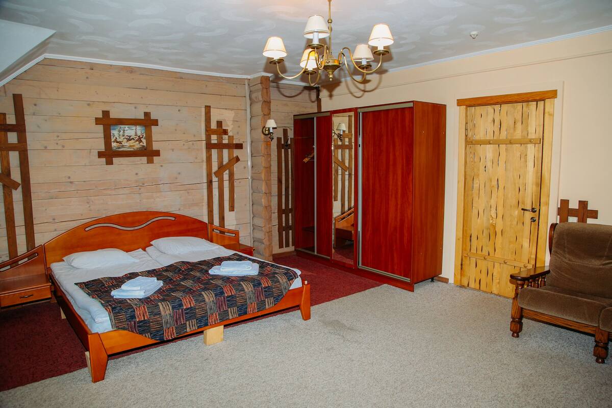 A bedroom with a wooden bed, a red wardrobe, a wooden chair, and a chandelier.