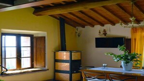 Ein Essbereich mit einem Holztisch, Stühlen, einer Topfpflanze, einem Fernseher und einem Fenster mit Vorhängen.