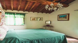 A bedroom with a bed, a chandelier, a window with curtains, and two framed pictures on the wall.
