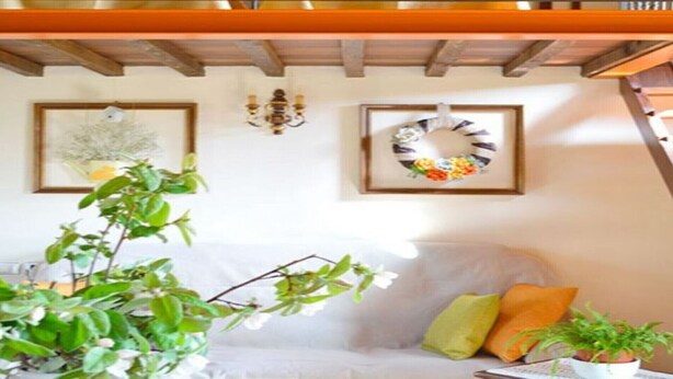 Ein gemütliches Wohnzimmer mit einem weißen Sofa, einer grünen Pflanze und einem bunten Kranz an der Wand.
