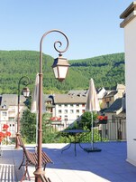Una terraza con mobiliario exterior, una lámpara colgante y vistas a una colina con edificios.