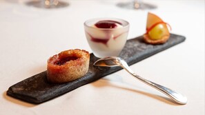 A dessert plate with a caramelized pastry, a glass of red jelly, and a fruit slice on a slate serving board. - Hôtel de France (Mende)