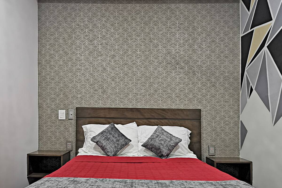 A bedroom with a patterned wallpaper, a wooden headboard, a red bedspread, and two nightstands with lamps.