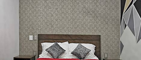 Un dormitorio con papel tapiz estampado, cabecera de madera, colcha roja y dos mesitas de noche con lámparas.