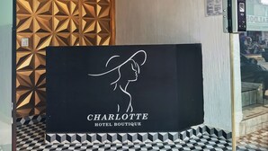 A reception area with a chandelier, geometric wall paneling, and a sign for 'Charlotte Hotel Boutique'.