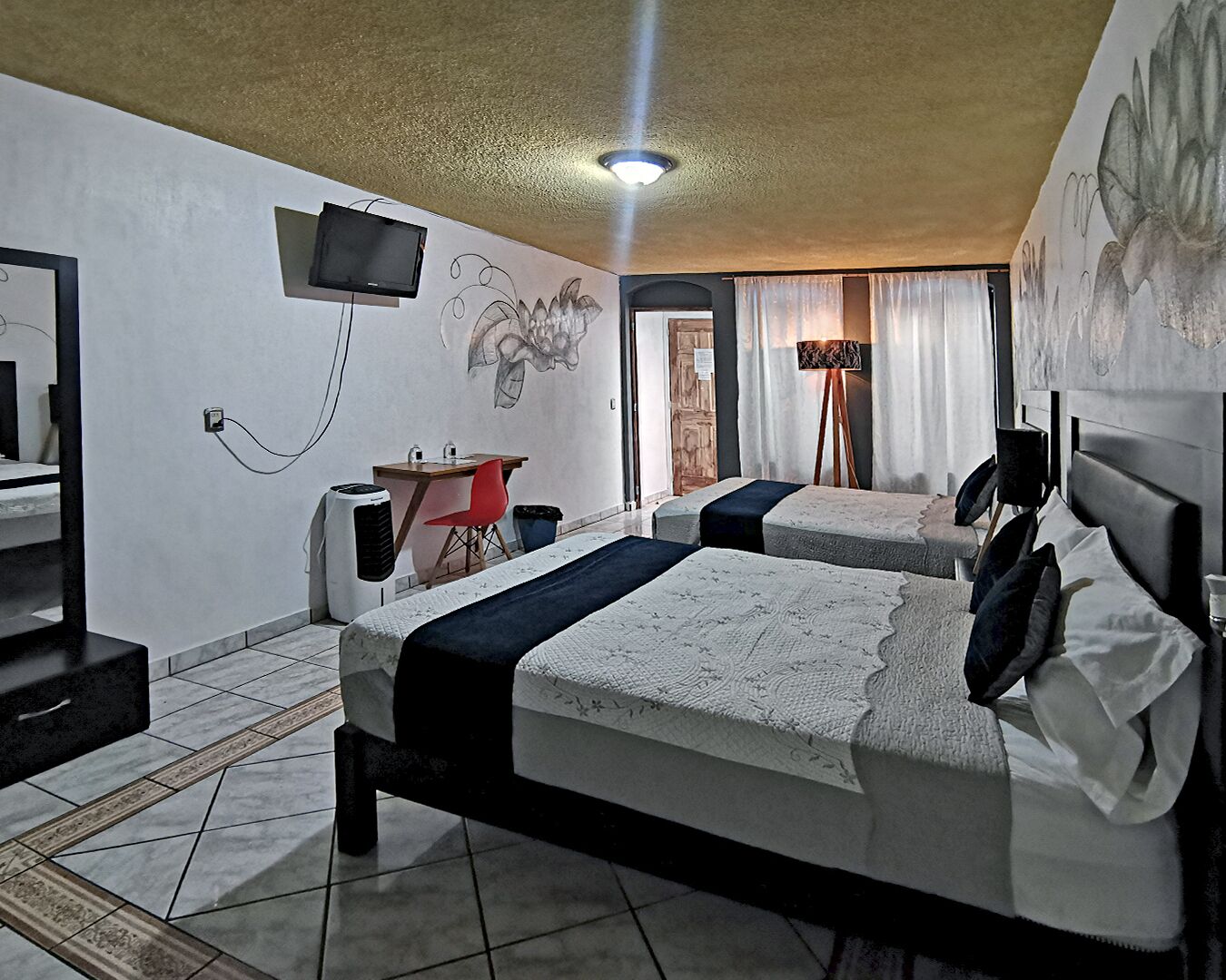 A hotel room with two beds, a desk with a chair, a TV mounted on the wall, and a painting on the wall.