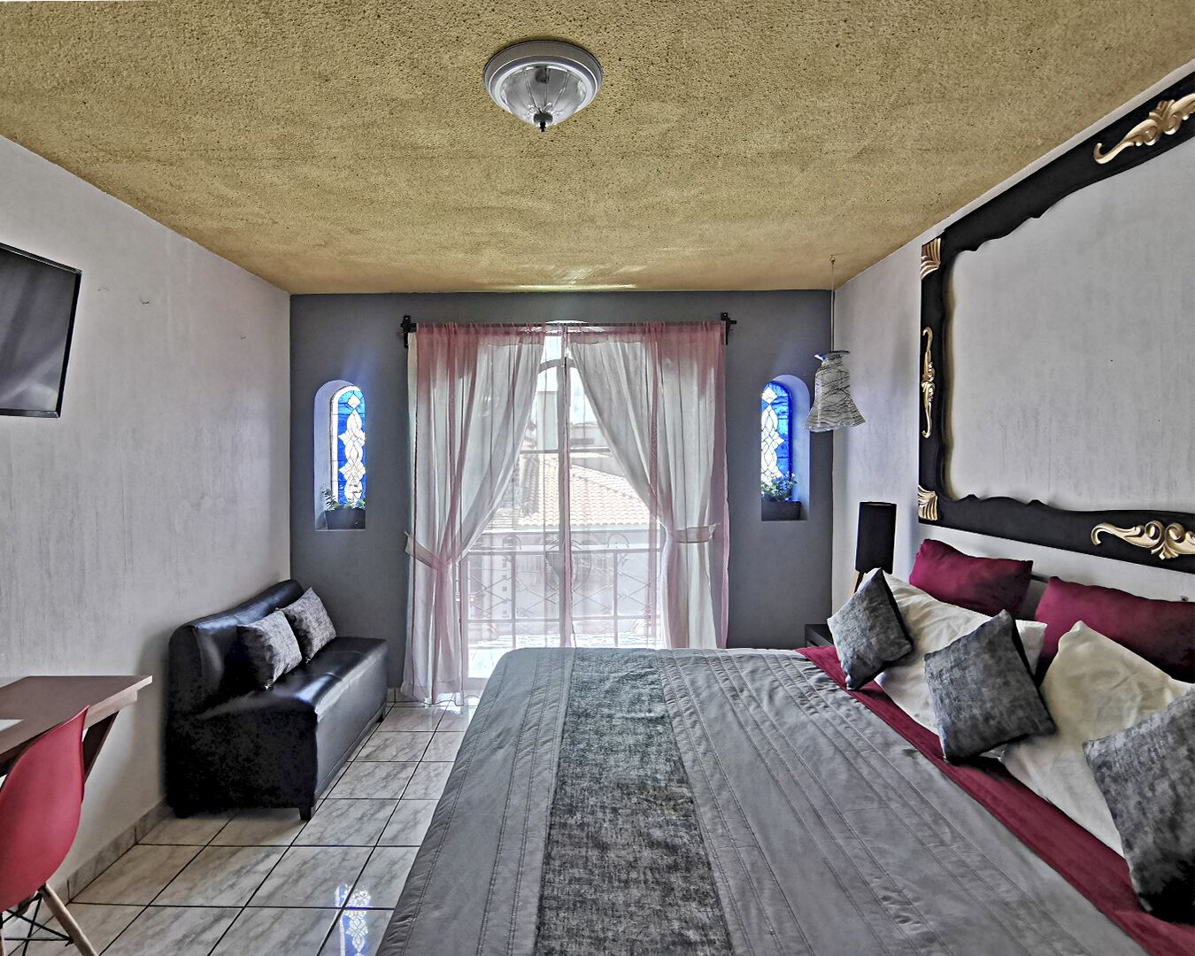 A bedroom with a large bed, a sofa, a desk, and two windows with curtains.
