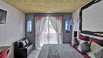 A bedroom with a large bed, a sofa, a desk, and two windows with curtains.