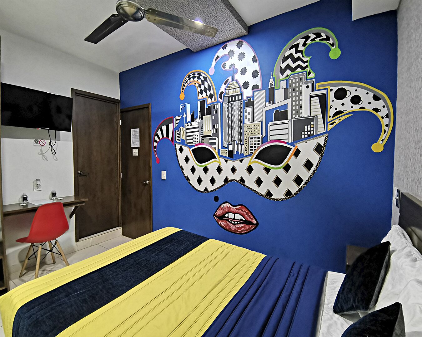 A bedroom with a cityscape mural, a bed with striped bedding, a red chair, and a ceiling fan.
