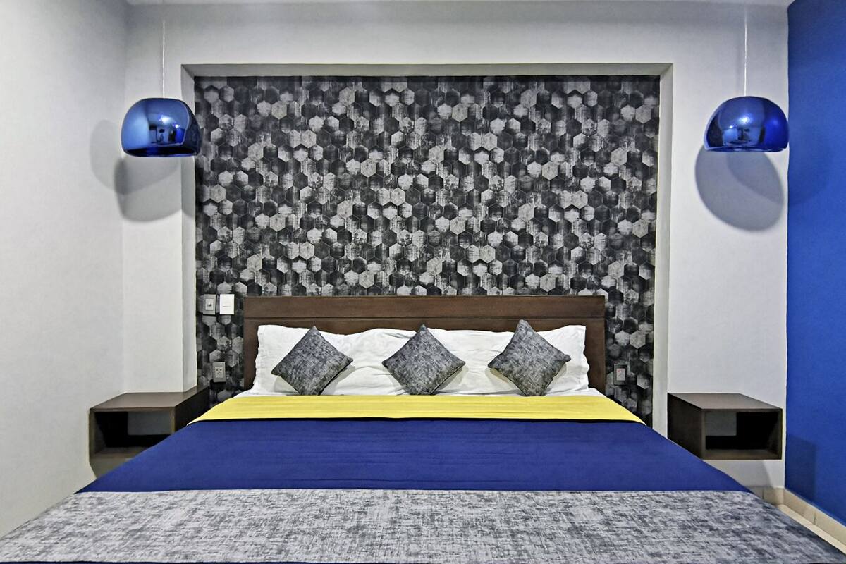 A neatly made bed with a blue and white bedspread, a wooden headboard, and a patterned wall behind it.