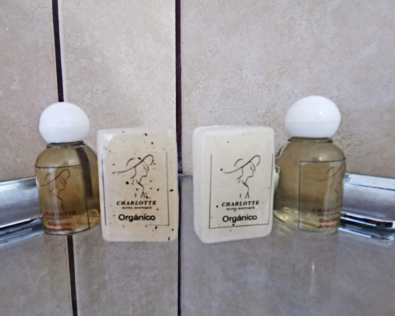 Três frascos de shampoo e condicionador Charlotte Organico sobre uma superfície azulejada.