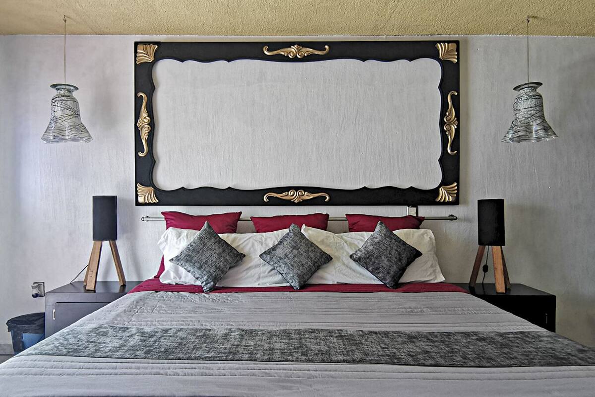 A neatly made bed with a black and gold headboard, red and grey pillows, and a grey bedspread.
