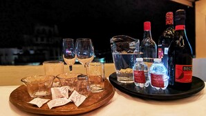 A tray with wine glasses, bottles, and water bottles on a table with a view of a cityscape.