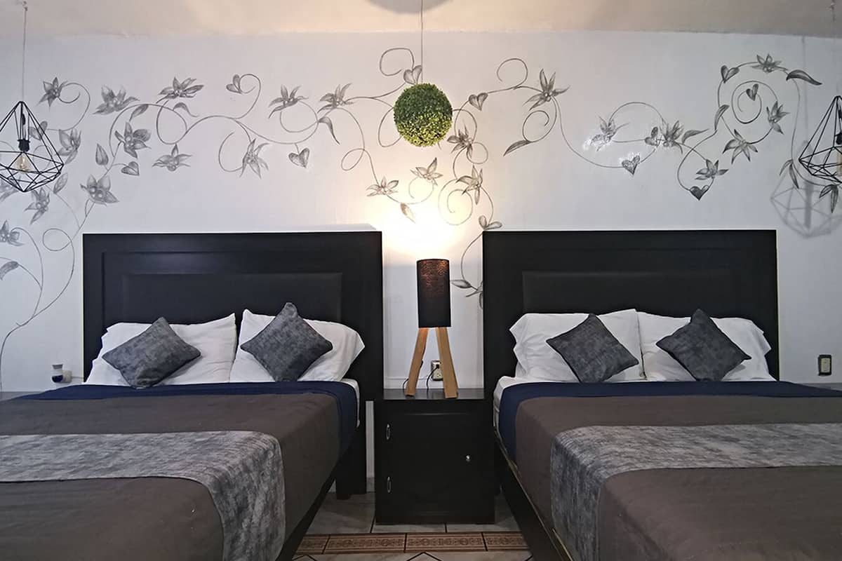A double room with two beds, a nightstand with a lamp, and a wall with floral and geometric designs.