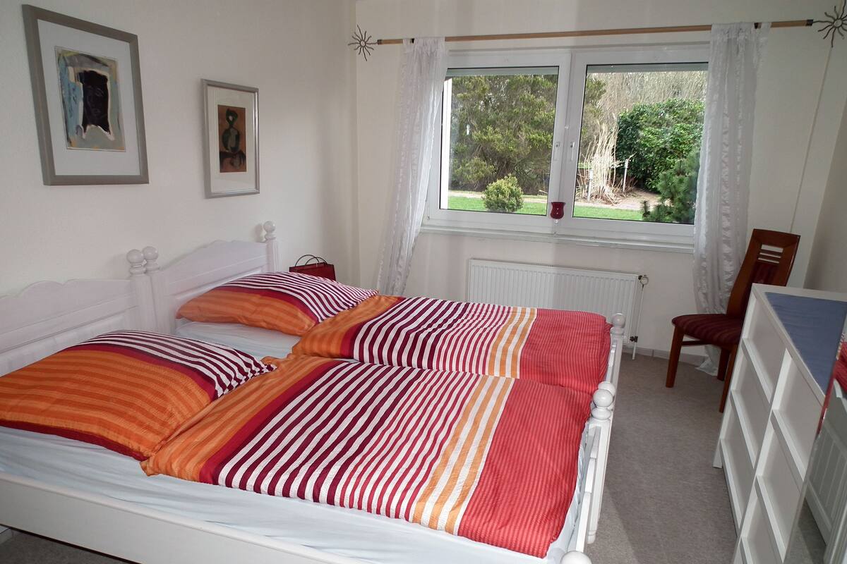 Une chambre à coucher avec un lit, une chaise, une fenêtre et deux tableaux encadrés accrochés au mur.