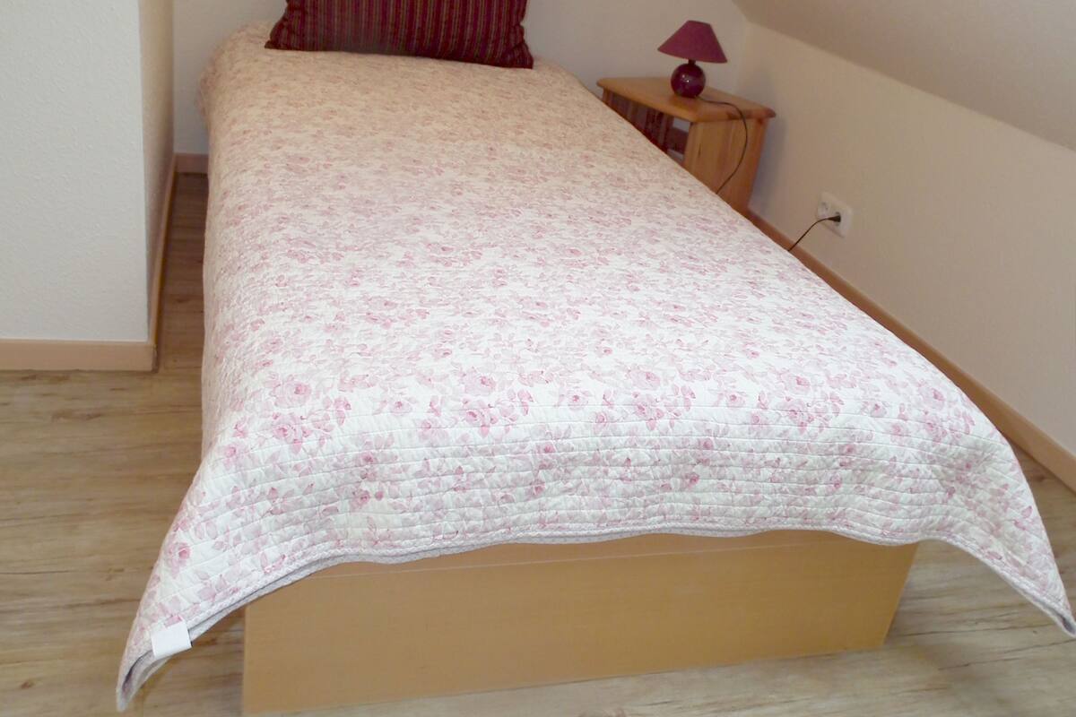 Une chambre à coucher avec un lit, une table de chevet, une lampe et un plancher en bois.