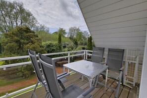 Uma varanda com mesa e cadeiras de metal, com vista para um jardim e um caminho de tijolos.