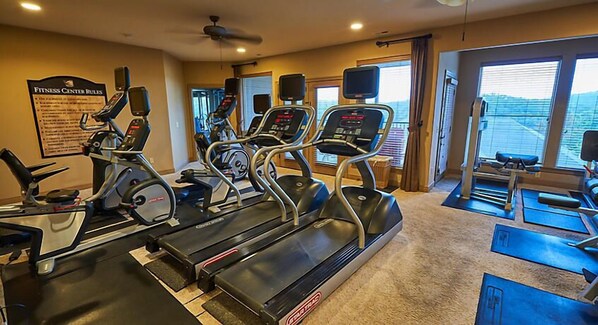 Un gimnasio con cintas de correr, elípticas y un espejo grande.