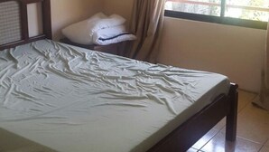 A single bed with a wooden frame and a white mattress in a room with beige walls and a tiled floor. - Apartment overlooking the volcano II (Santa Rosa)