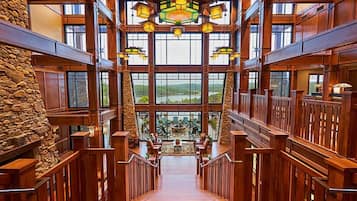 A spacious interior with a central staircase, wooden railings, and large windows offering a view of the outdoors.