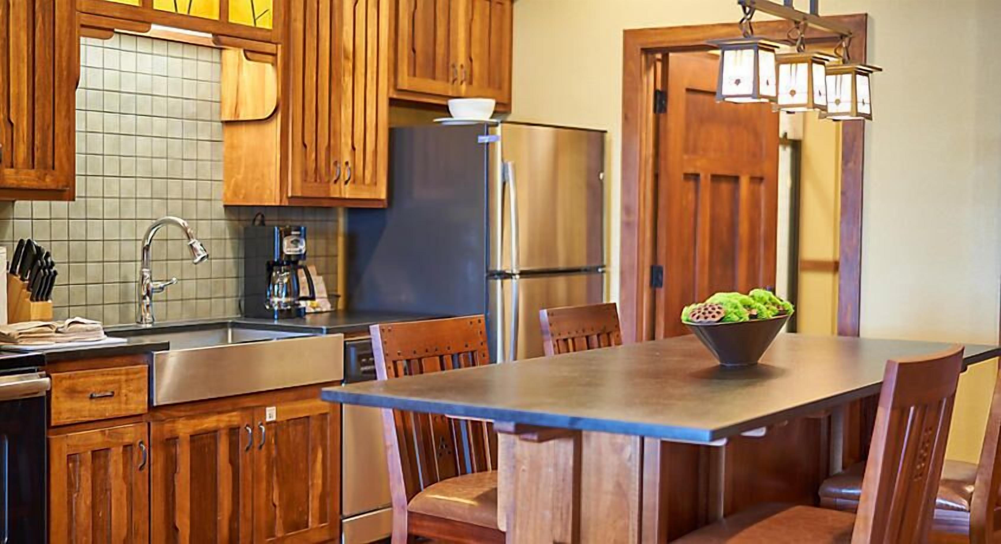 A kitchen with wooden cabinets, a stainless steel refrigerator, a sink, and a dining table with chairs.