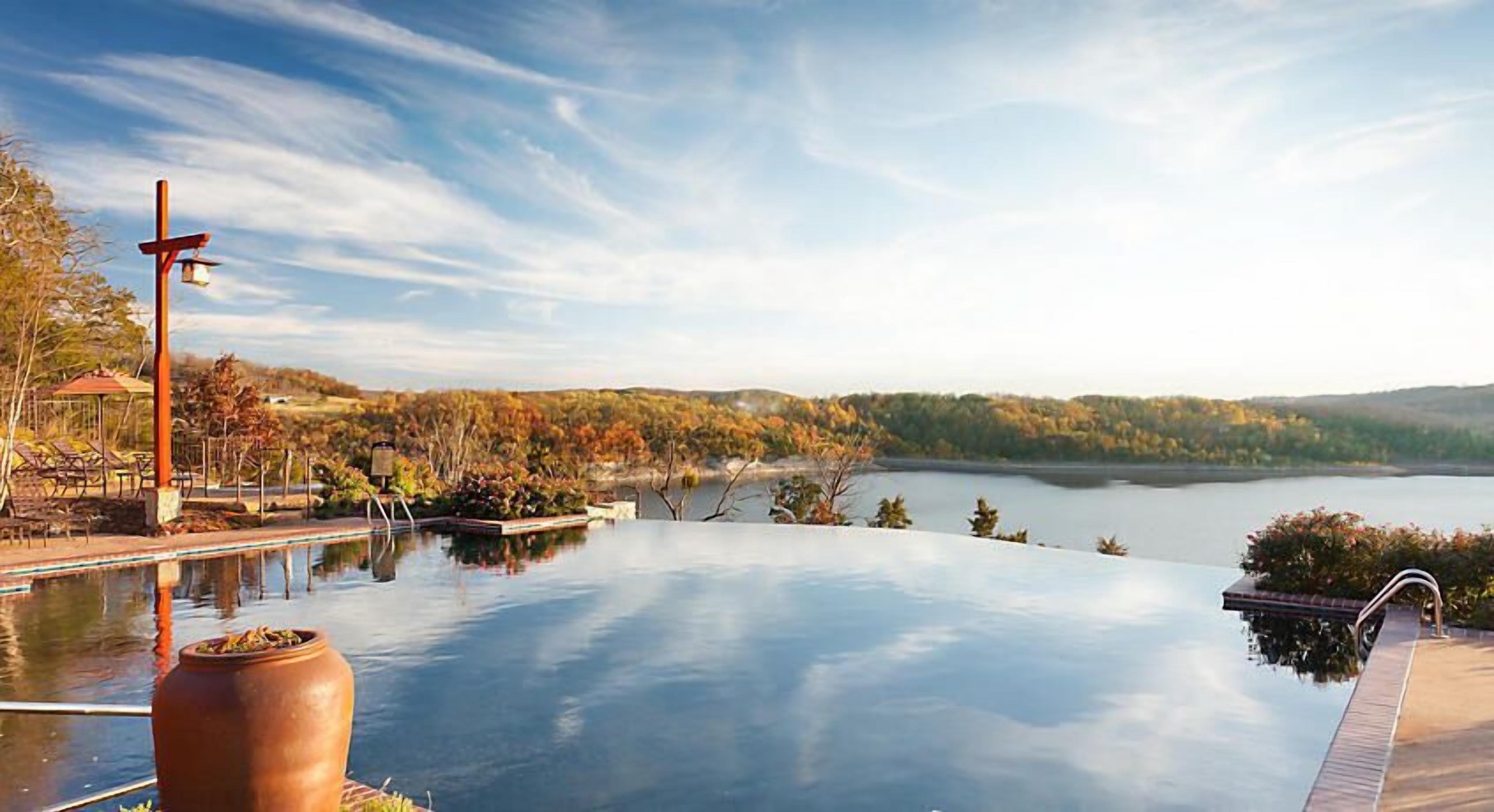 An infinity pool with a view of a lake and autumn foliage.