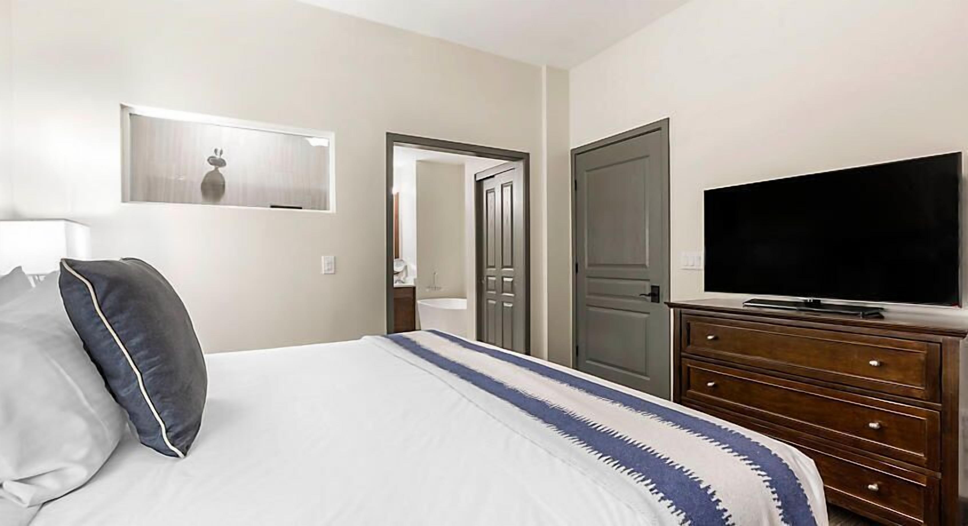 A hotel room with a bed, a TV, a dresser, and a door leading to a bathroom.