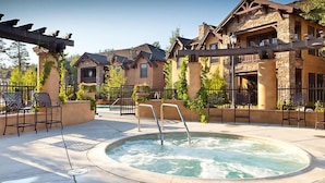 Ein Whirlpool, umgeben von Sitzgelegenheiten im Freien, ein Steinhaus und eine Pergola.