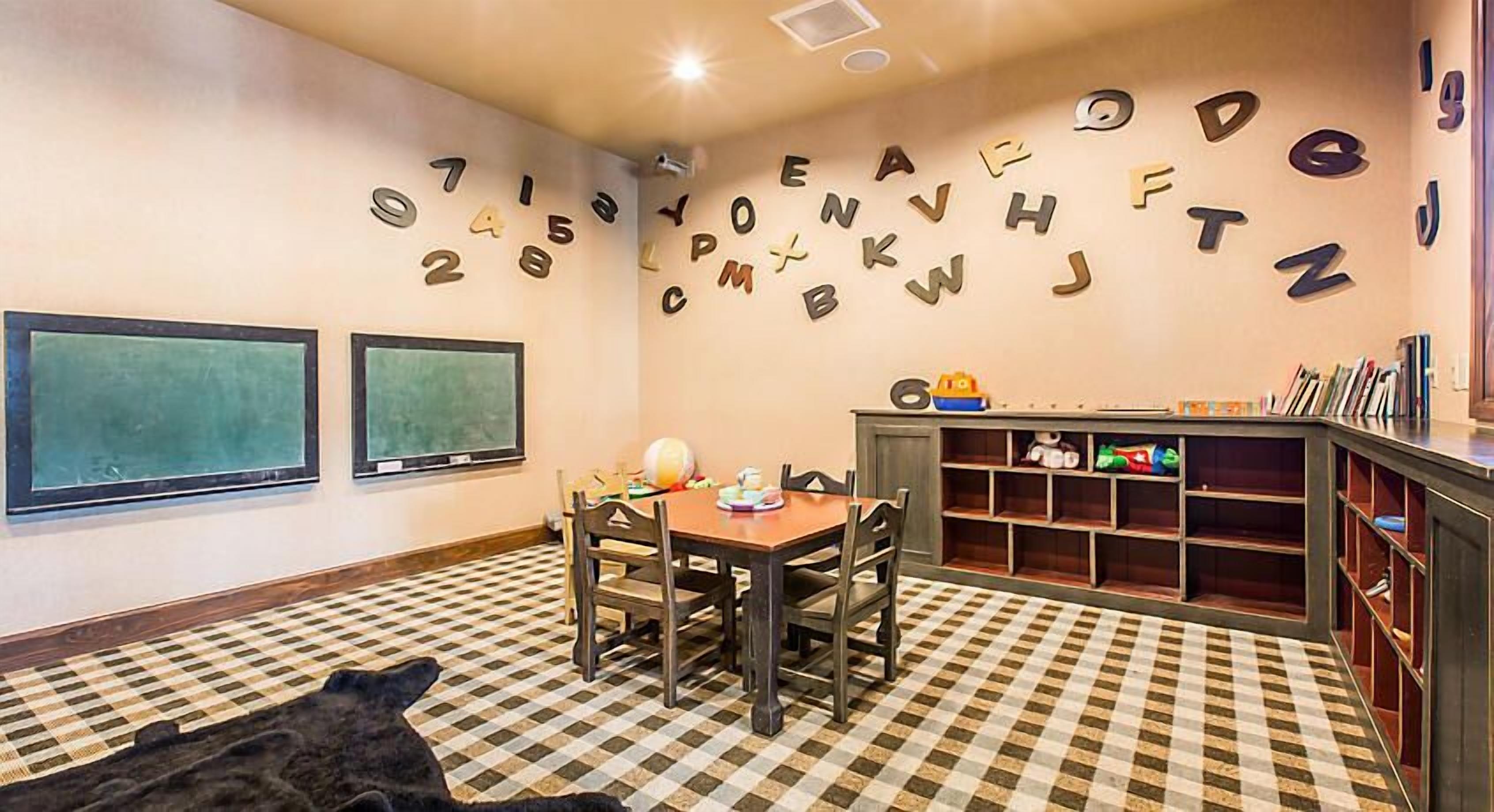 Una habitación con piso a cuadros, una mesa con sillas, una estantería y letras del alfabeto en la pared.
