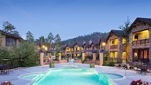 Ein Resort mit einem zentralen Pool, mehreren Gästezimmern mit Balkonen und einer Bergkulisse.