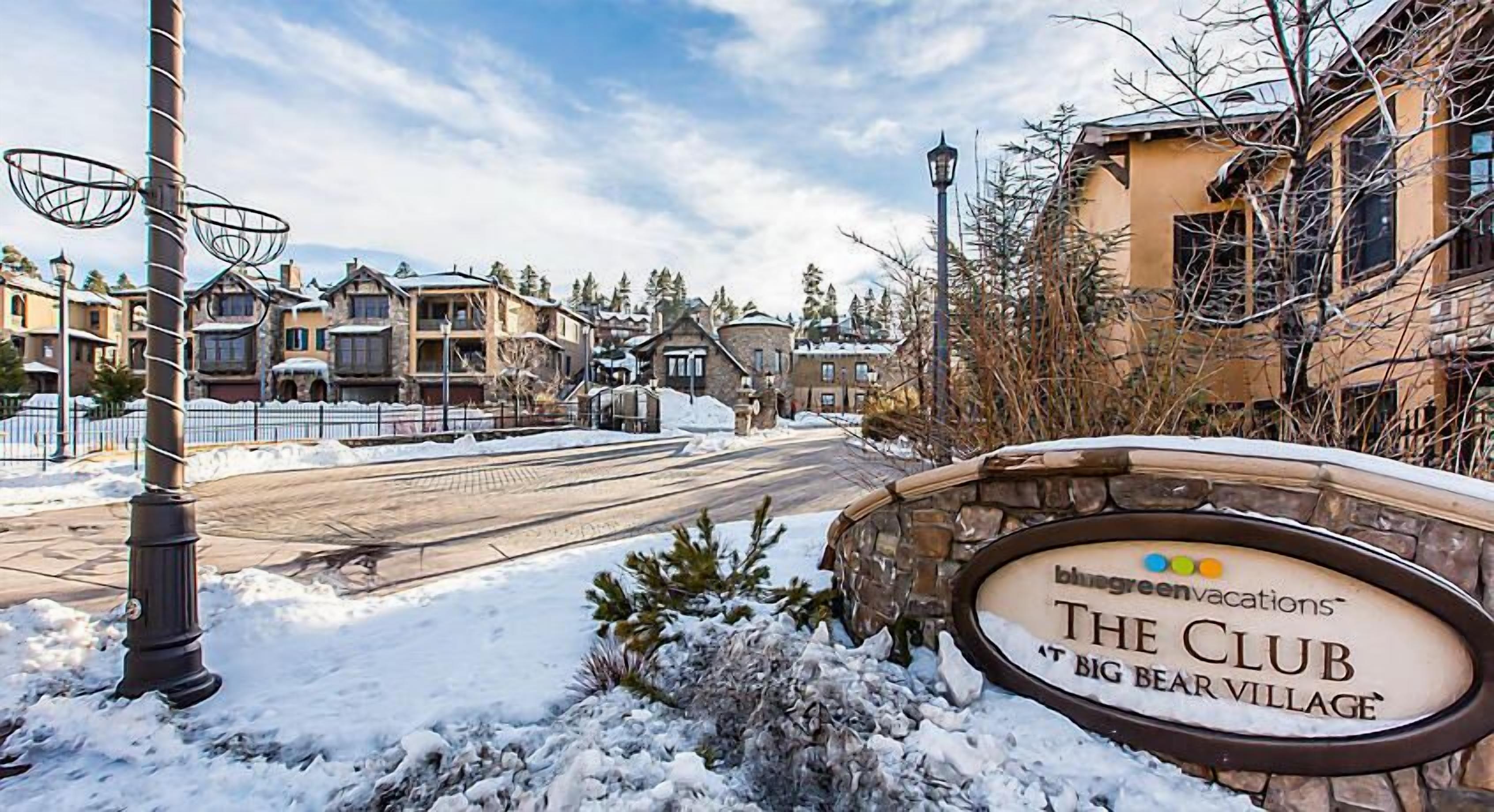 A snow-covered street with a sign for 'The Club at Big Bear Village'.